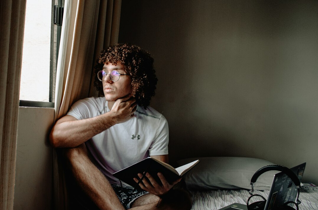 Brazilian man reading a book by a window during a quiet morning